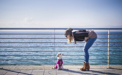 Volle Länge Seitenansicht der jungen Frau durch Geländer vor dem Meer beugte sich über Blick auf Hund - CUF15175