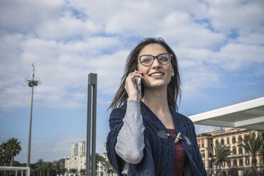 Niedriger Blickwinkel einer jungen Frau mit Brille, die ein Smartphone benutzt und lächelnd wegschaut - CUF15177