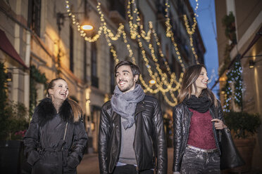 Low angle front view of friends walking down street in the evening smiling - CUF15178