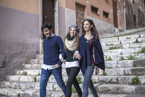 Friends walking down stone steps arm in arm smiling - CUF15191