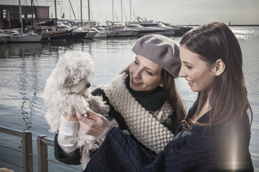 Young women in boatyard holding up dog smiling - CUF15192