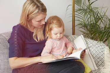 Woman and toddler daughter reading on living room sofa - CUF15198