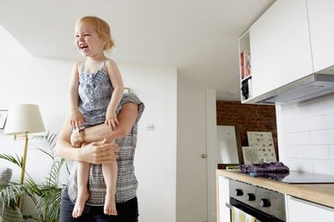 Woman lifting up toddler daughter in kitchen - CUF15215