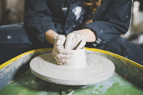 Cropped view of young woman sitting at pottery wheel making clay pot - CUF15226