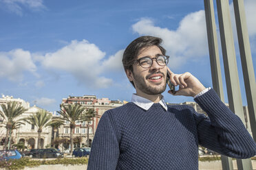 Junger Mann mit Brille, der ein Smartphone benutzt und lächelnd wegschaut - CUF15273