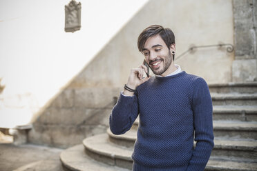 Young man in front of stone steps using smartphone smiling - CUF15281