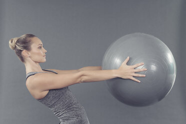 Junge Frau trainiert mit Gymnastikball, grauer Hintergrund - CUF15282