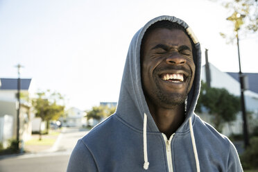 Portrait of man wearing hooded top eyes closed laughing - CUF15287