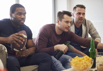 Gruppe von Männern, die einen Ball halten und mit Snacks und Bier ein Sportereignis im Fernsehen verfolgen - CUF15439