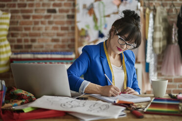 Frau im Designstudio sitzt am Schreibtisch und skizziert Modedesign - CUF15445