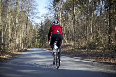 Rückansicht einer Radfahrerin auf einer von Bäumen gesäumten Straße - CUF15481