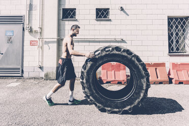 Junger männlicher Crosstrainer, der einen großen Reifen vor einem Fitnessstudio schiebt - CUF15617