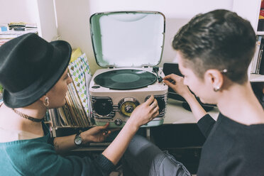 Blick über die Schulter auf zwei junge Frauen, die Vinyl auf einem alten Plattenspieler spielen - CUF15657