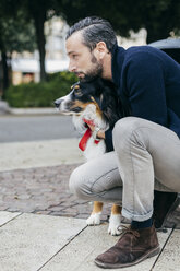 Mid adult man crouching with pet dog on city sidewalk - CUF15680