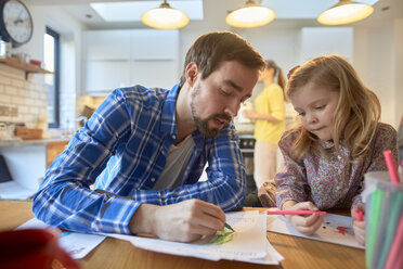 Mid adult man and daughter colouring at table in kitchen - CUF15715