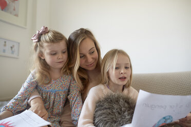 Mid adult woman looking at drawings with daughters in living room - CUF15722