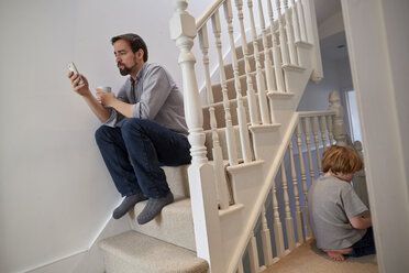 Junge und Vater sitzen auf der Treppe, Vater liest Smartphone-Texte - CUF15726