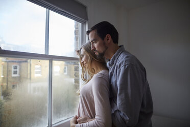Mid adult couple gazing out through bedroom window - CUF15730