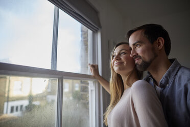 Mid adult couple looking out through bedroom window - CUF15731
