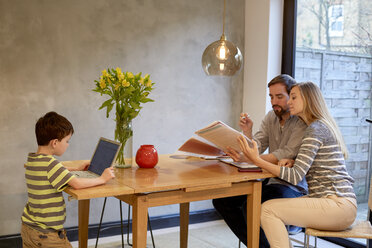Mid adult couple looking at paperwork on dining table whilst son uses laptop - CUF15736