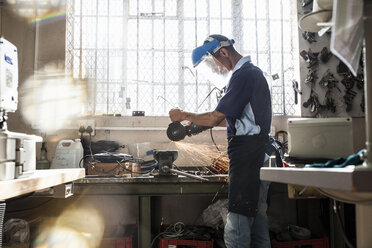 Junger Mann mit Winkelschleifer am Schraubstock in einer Reparaturwerkstatt - CUF15740