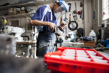 Junger Mann mit Winkelschleifer am Schraubstock in einer Reparaturwerkstatt - CUF15741