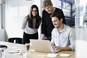 Colleagues in office using laptop smiling - CUF15757