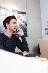 Man in office using mobile phone, looking away smiling - CUF15764