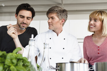 Chef and couple in kitchen tasting food - CUF15776