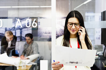 Junge Frau im Büro mit Papierkram und Mobiltelefon - CUF15807