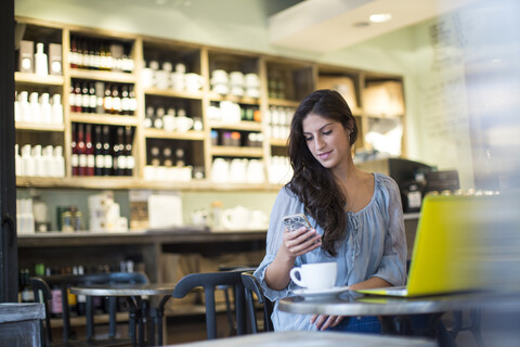 Junge Frau liest Smartphone-Texte in einem Café, lizenzfreies Stockfoto