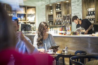 Junge Frau schaut in einem Café auf ein digitales Tablet - CUF15852
