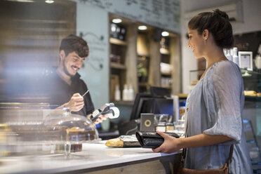 Barista beim Berechnen der Rechnung für eine Kundin an der Kaffeetheke - CUF15855