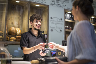 Barista übergibt Kreditkarte an weibliche Kundin an der Kaffeetheke - CUF15858