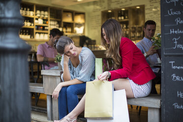 Zwei junge Freundinnen mit Einkaufstaschen unterhalten sich vor einem Café - CUF15860
