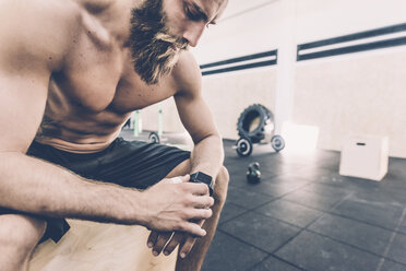 Young man sitting checking smartwatch in cross training gym - CUF15880