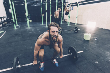 Young male cross trainer preparing to lift barbell in gym - CUF15881