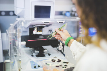 Female scientist using FTIR spectrophotometer, positioning thin film sample on microscope stage - CUF15911