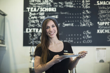 Porträt einer jungen Kellnerin mit Teller und Kuchenstück in einem Café - CUF15946