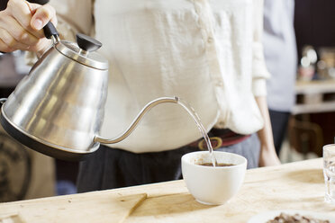 Kaffeeverkoster gießt heißes Wasser in eine Tasse Kaffee - CUF15967