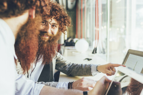 Männliche erwachsene Hipster-Zwillinge, die auf einen Laptop im Büro zeigen, lizenzfreies Stockfoto