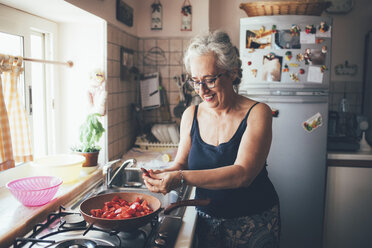 Frau hackt Tomaten in Topf lächelnd - CUF16053