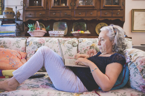 Frau auf dem Sofa liegend mit Laptop - CUF16058