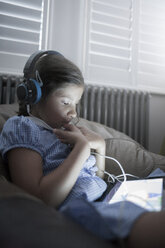 Schulmädchen sitzt auf dem Sofa, benutzt ein digitales Tablet und hört Kopfhörer - CUF16084