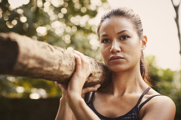 Porträt einer trainierenden Frau, die im Park einen Baumstamm auf die Schulter nimmt - CUF16089