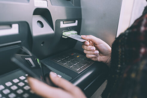 Hand einer jungen Frau, die eine Kreditkarte in einen Geldautomaten einführt - CUF16090
