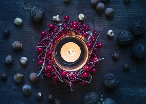 Draufsicht auf eine brennende Kerze, umgeben von Beerenkranz und Nüssen, lizenzfreies Stockfoto
