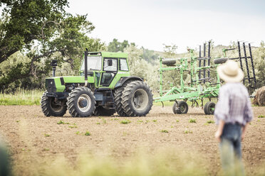 Jugendlicher beobachtet Landwirt beim Fahren eines Traktors auf einem gepflügten Feld - CUF16152