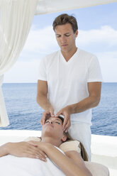 Männlicher Masseur gibt einer jungen Frau eine Kopfmassage am Strand, Mallorca, Spanien - CUF16178