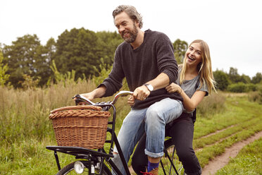 Porträt eines lachenden Paares beim Fahrradfahren auf einem ländlichen Feldweg - CUF16273
